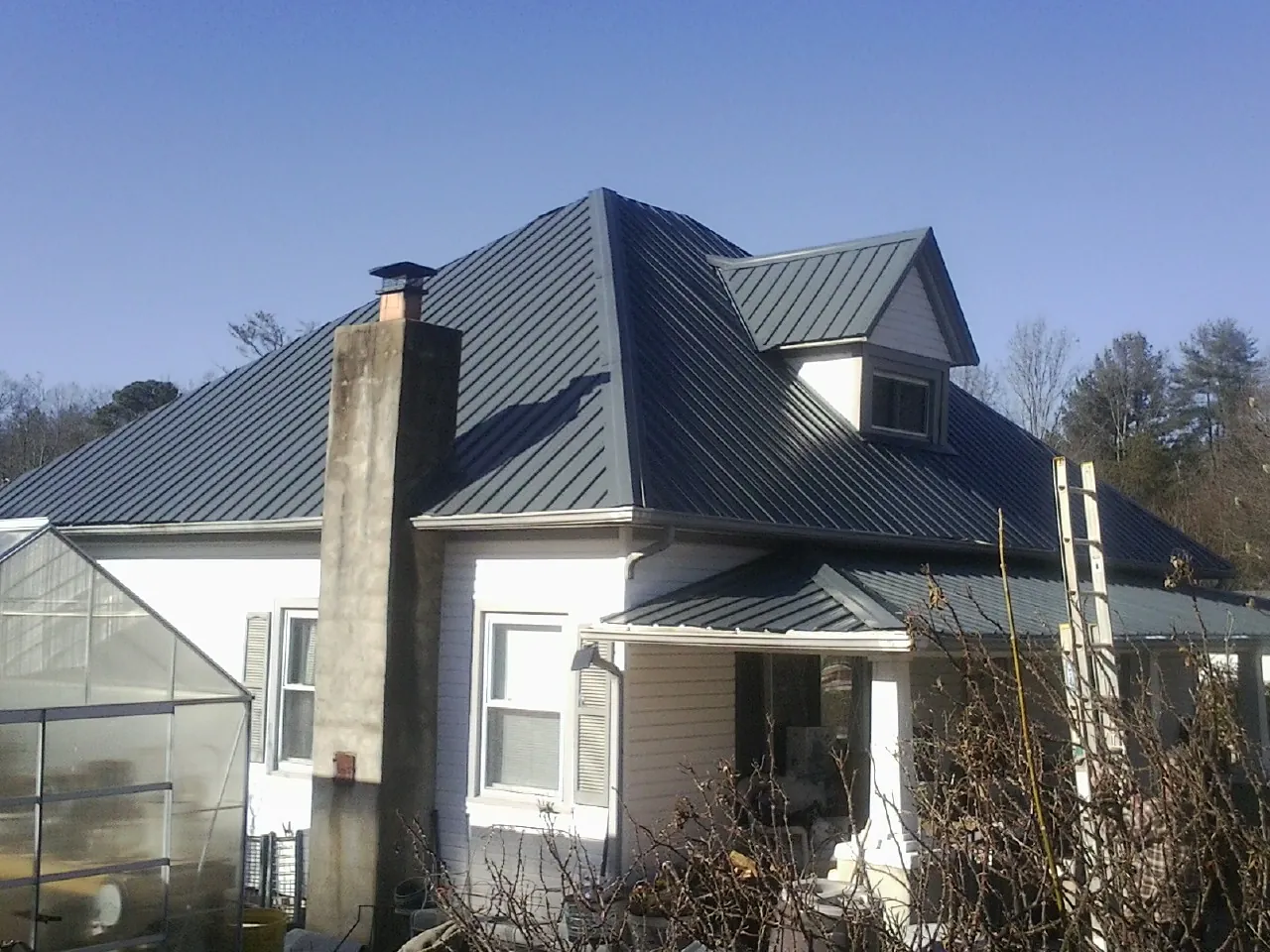 Dark blue standing seam metal roof on a white farmhouse with dormer — Slate & Tile Roof Repair by Roofing Brothers in Pownal