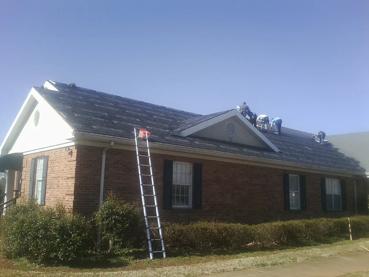 Crew tearing shingles off a brick ranch roof with a ladder set — Emergency Roof Repair work by our crew in Pownal