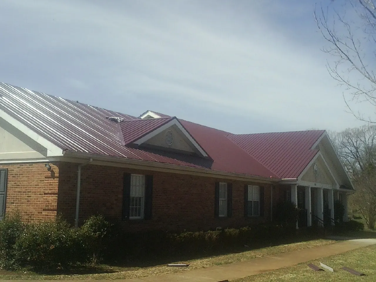 Red metal roof with gabled entries on a long brick building, from a Hail Damage Roof Repair job in Pownal