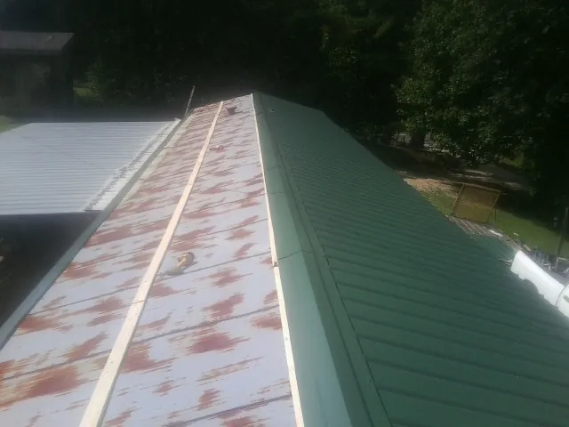 Old rusted panels beside newly installed green metal roofing — Wind Damage Roof Repair by Roofing Brothers in Pownal