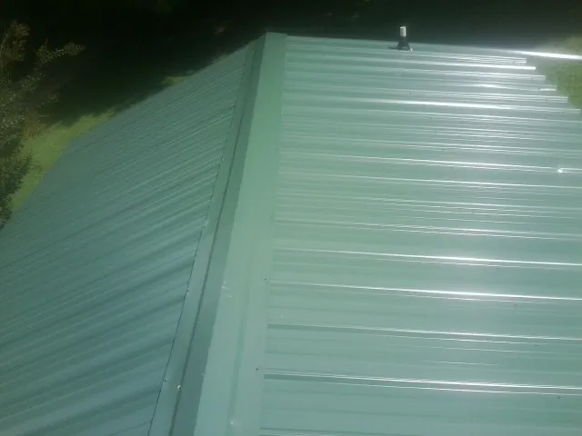 New green metal panels meeting at the ridge of a roof — Flat Roof Repair work by our crew in Pownal