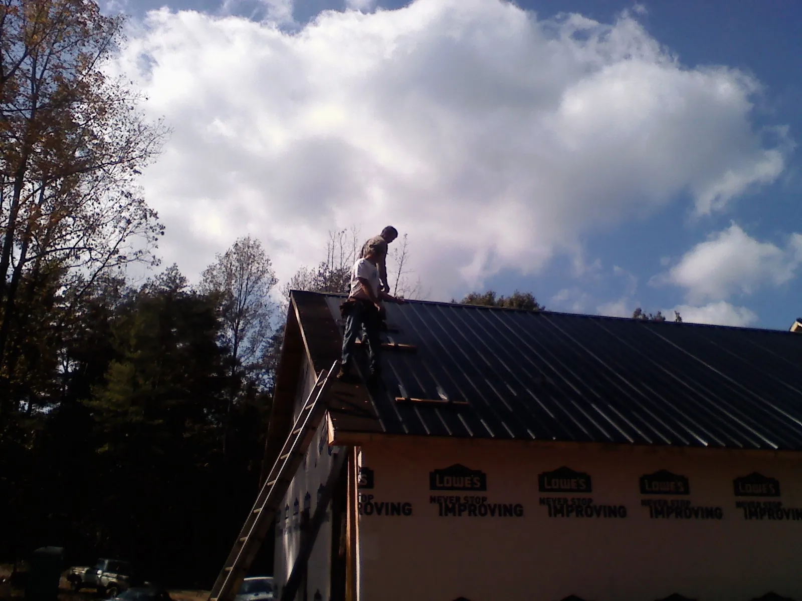 Roofer fastening dark metal panels high against a cloudy sky, from a Roof Inspection job in Pownal