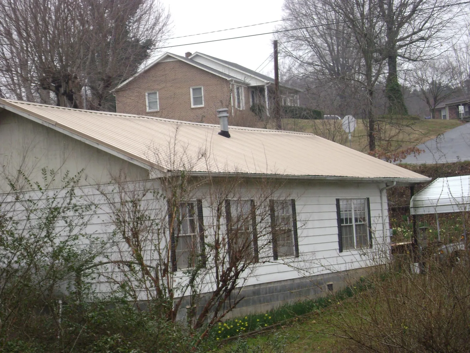 Tan metal roof on a white sided house set into a hillside — Commercial Roofing by Roofing Brothers in Pownal